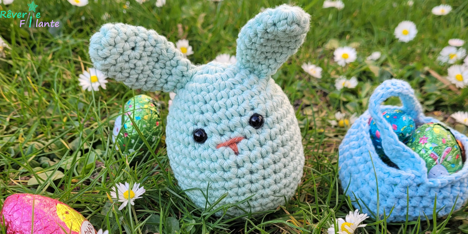 Small crocheted green bunny on the grass surrounded by chocolate Easter eggs