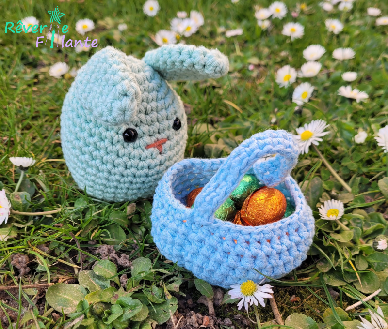 Small crocheted green bunny on the grass with a basket full of chocolate Easter eggs